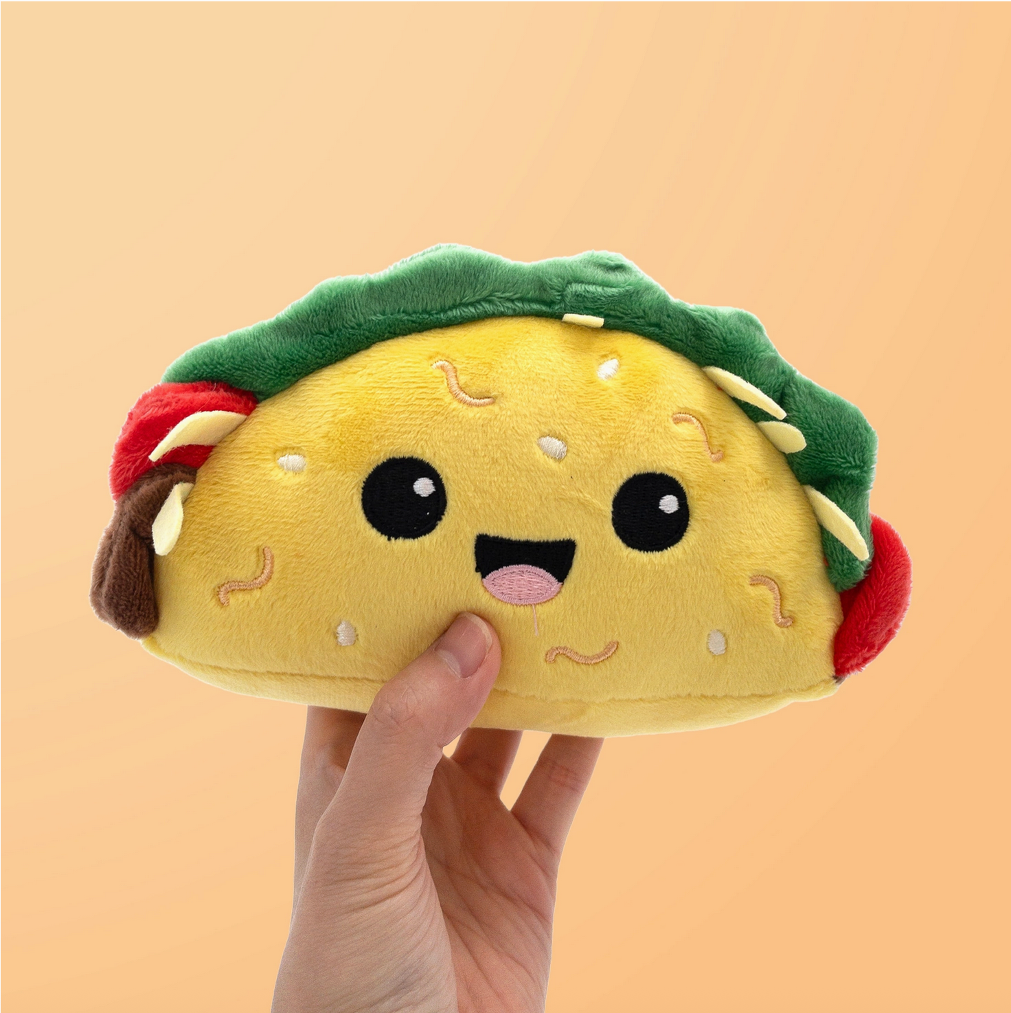 Plush taco toy held by a hand against a beige background - Little-ish