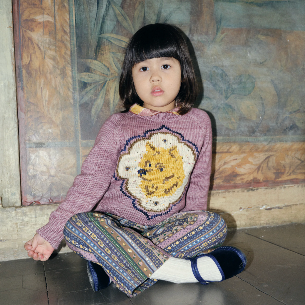 Child wearing a sweater with a lion design sitting on the floor.