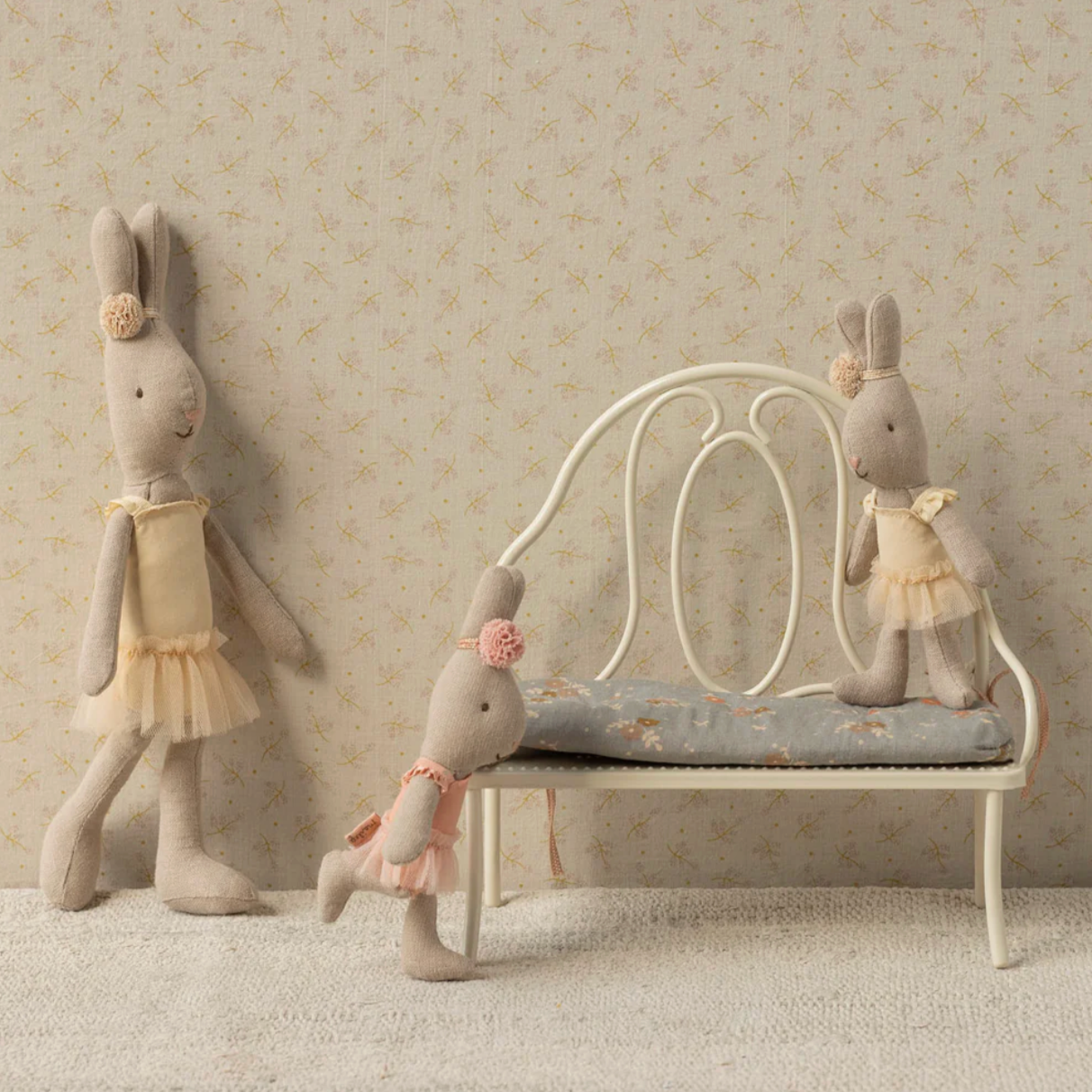 Three plush rabbit toys in a decorative setting with a bench and wallpaper. - Little-ish