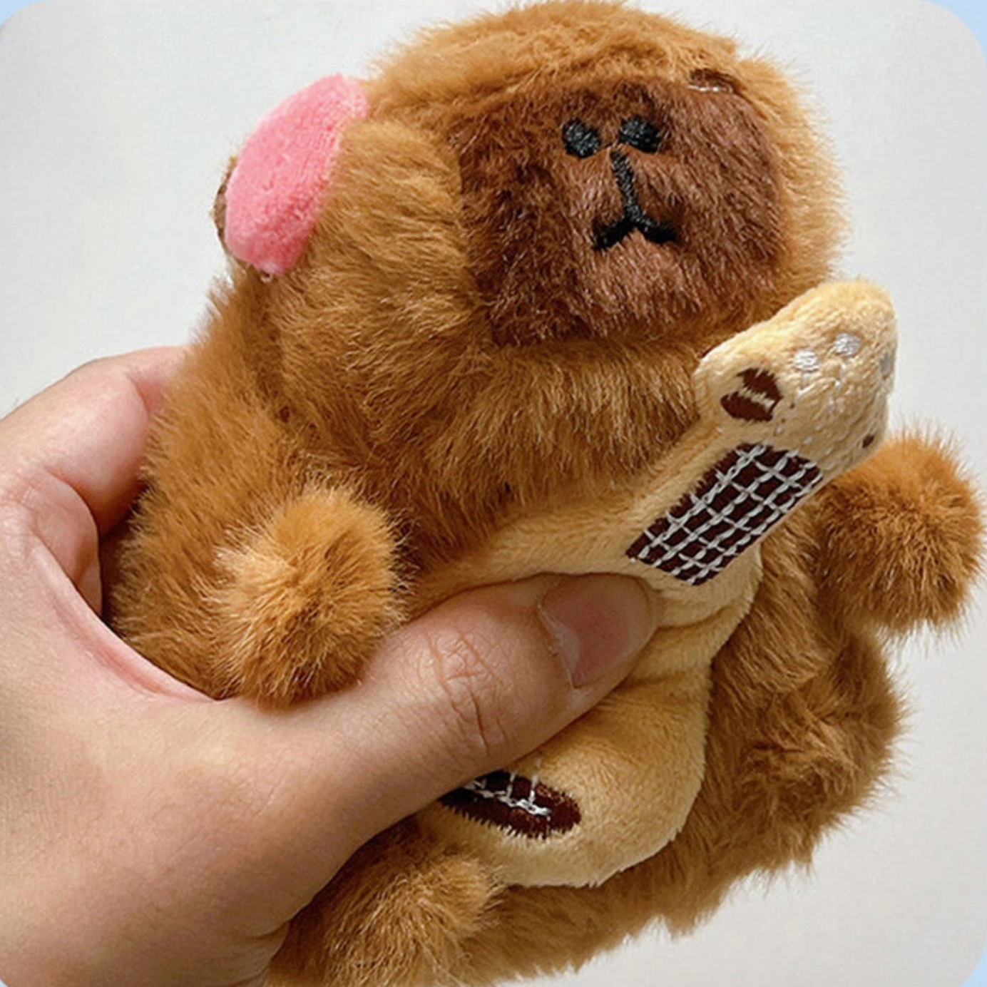 Plush monkey toy held in a hand against a light blue background - Little-ish