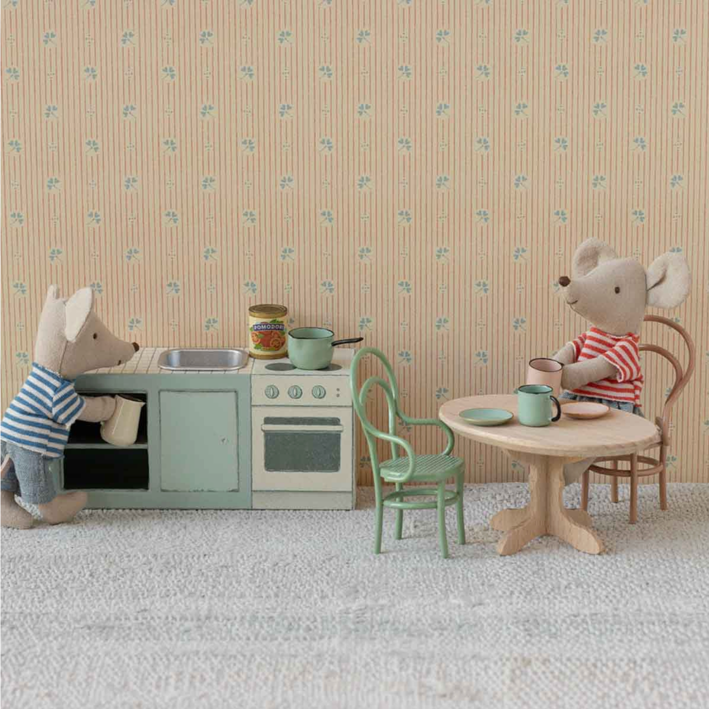 Children's play kitchen set with toy animals in a room with floral wallpaper.
