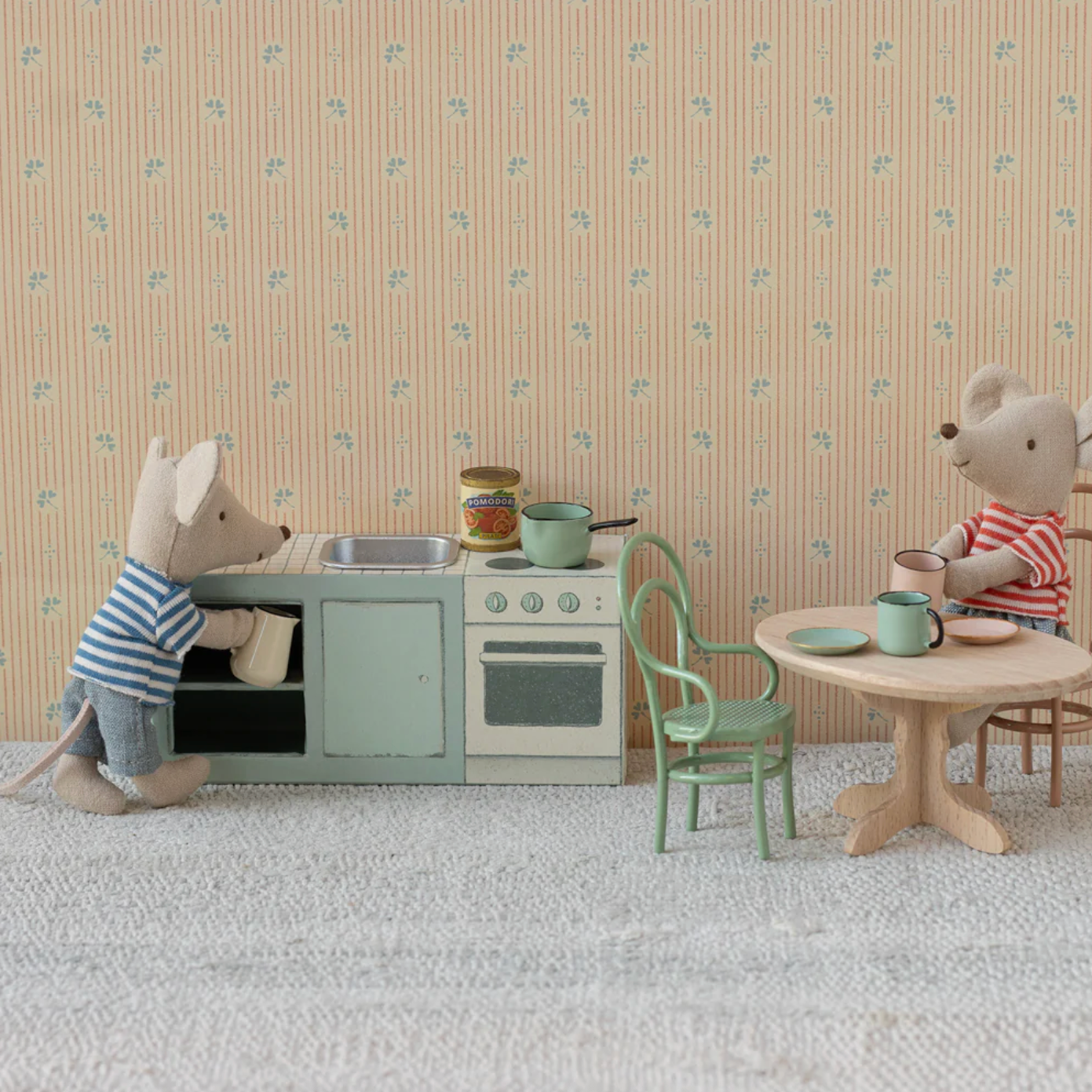 Two toy mice in a miniature kitchen setting with a patterned wall background.