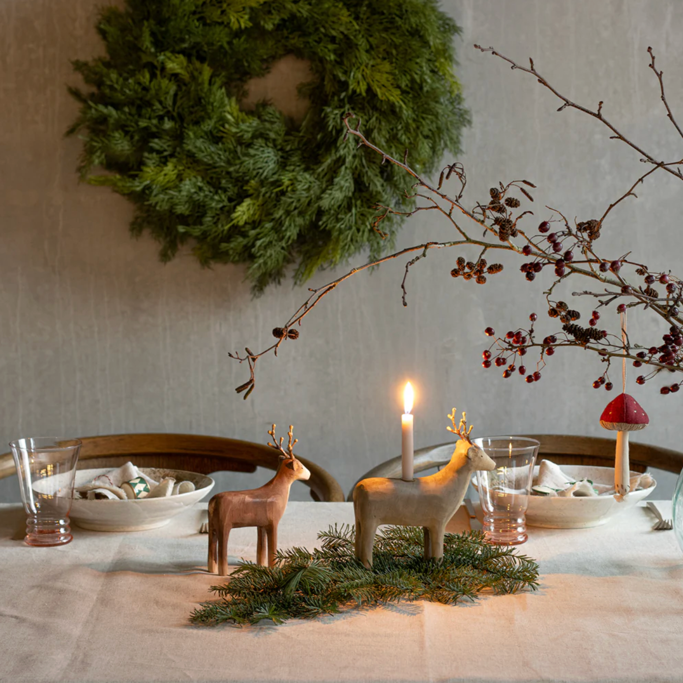 Dining table set with Christmas decorations including reindeer figurines, a candle, and a wreath on the wall.