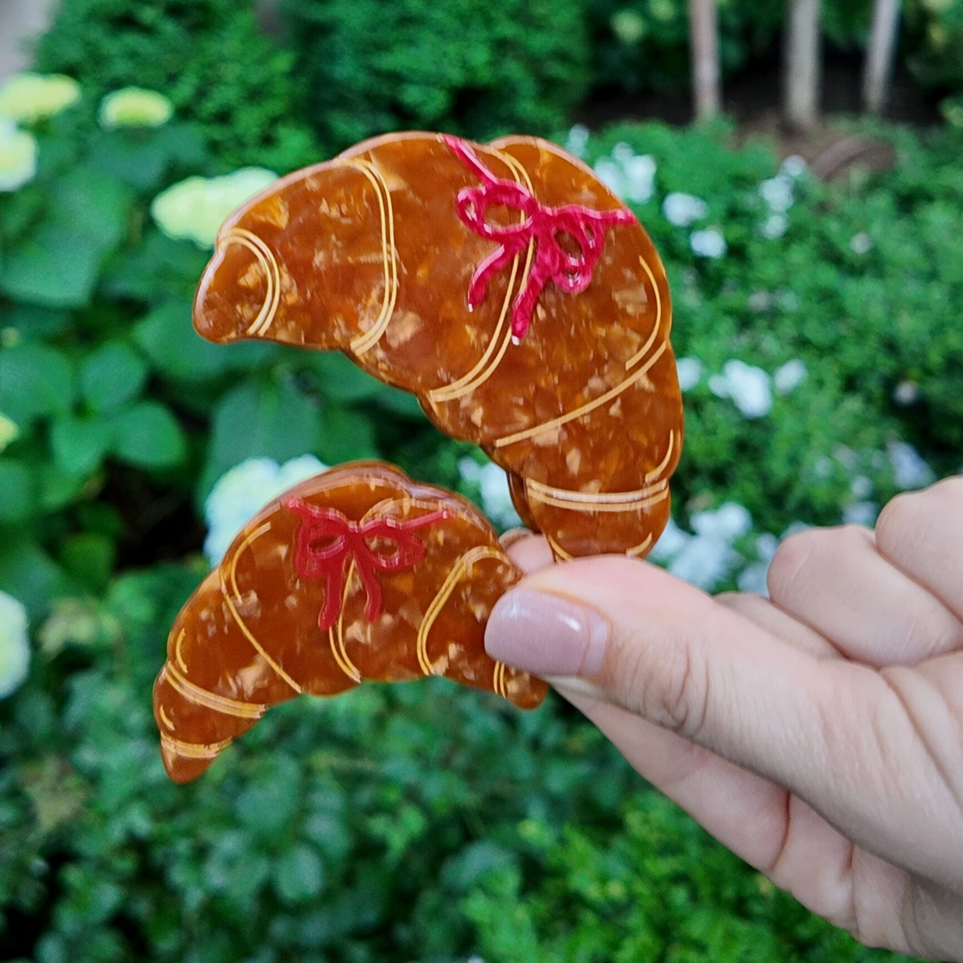 Hand holding a croissant-shaped cookie with a pink bow against a garden background