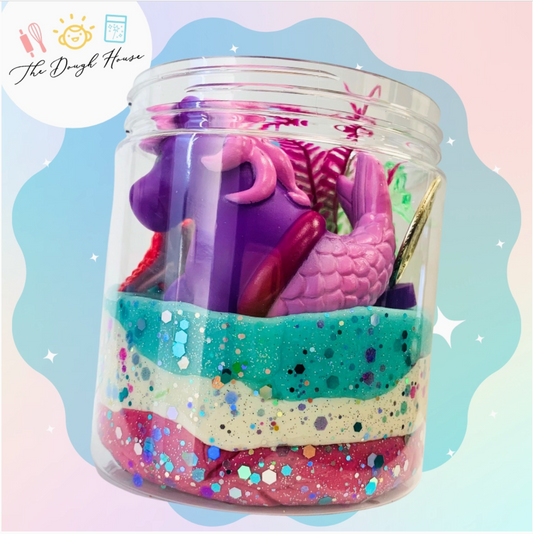 Colorful jar filled with toys and glittery sand, branded 'The Dough House'.