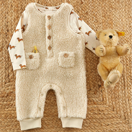 Baby romper with button details and teddy bear on a textured surface