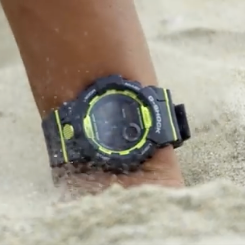 Digital watch with a black and yellow strap on a sandy background