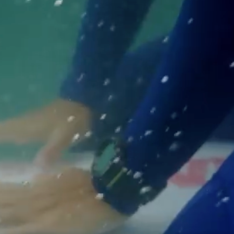 Close-up of a person's hand underwater with a blue sleeve and watch.