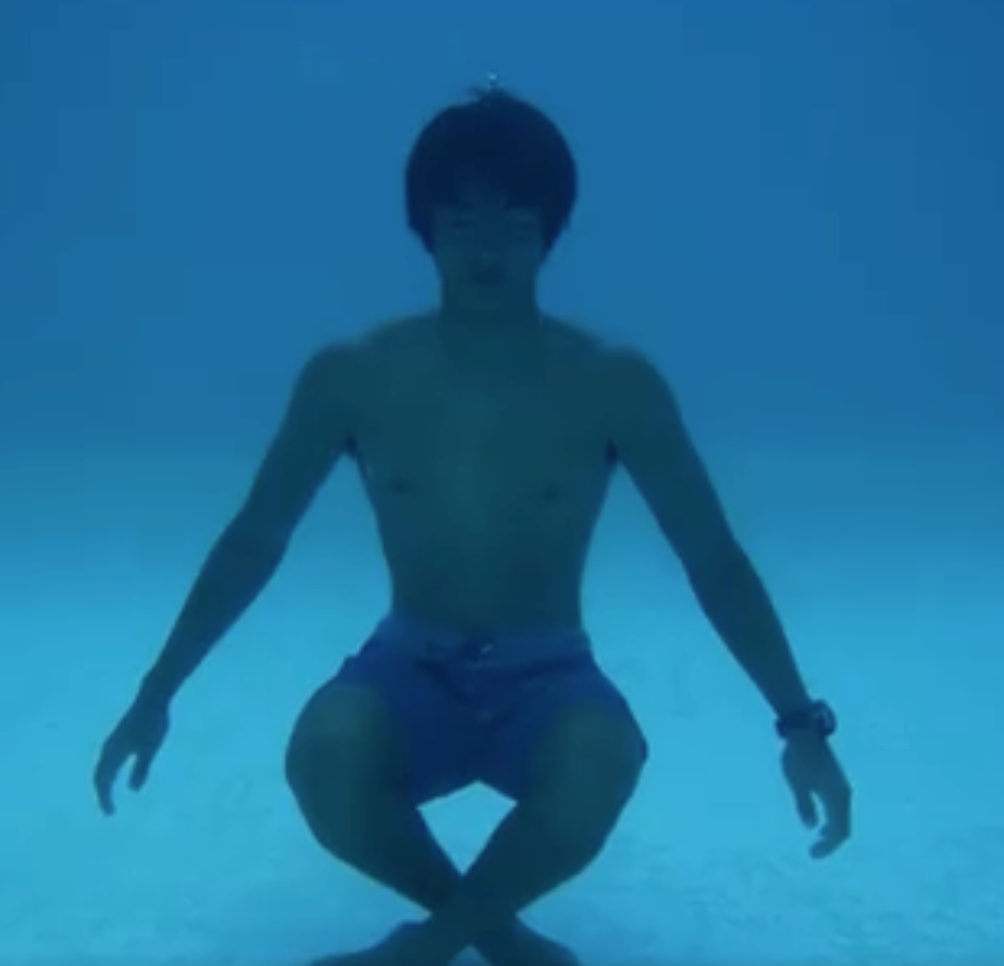 Person underwater wearing blue swim shorts in a pool