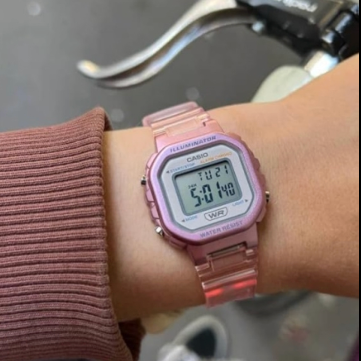 Pink Casio digital watch on a wrist with a blurred background