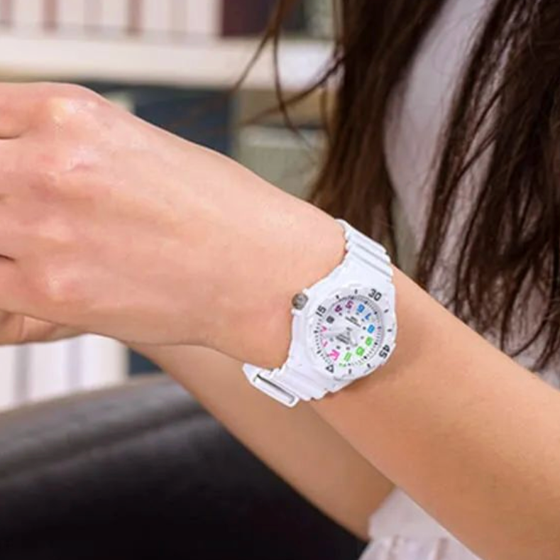 White digital watch with colorful display on a wrist against a blurred indoor background
