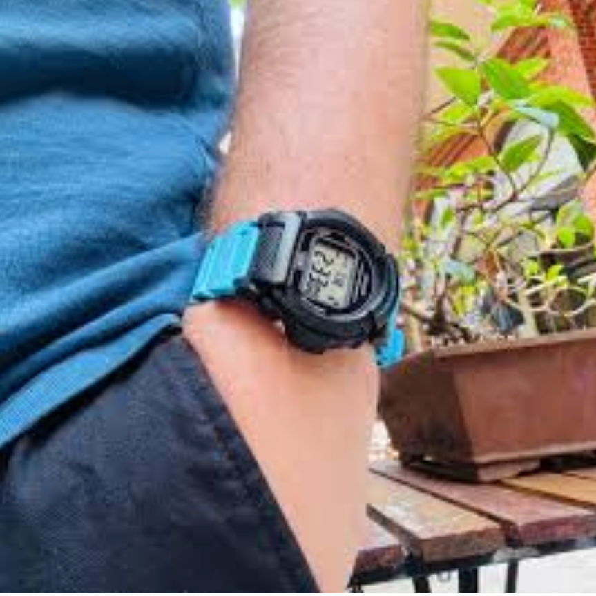 Person wearing a black digital watch with a blue strap, sitting outdoors.