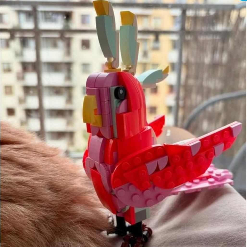 Lego parrot-shaped toy made of interlocking bricks held by a person with a blurred background.