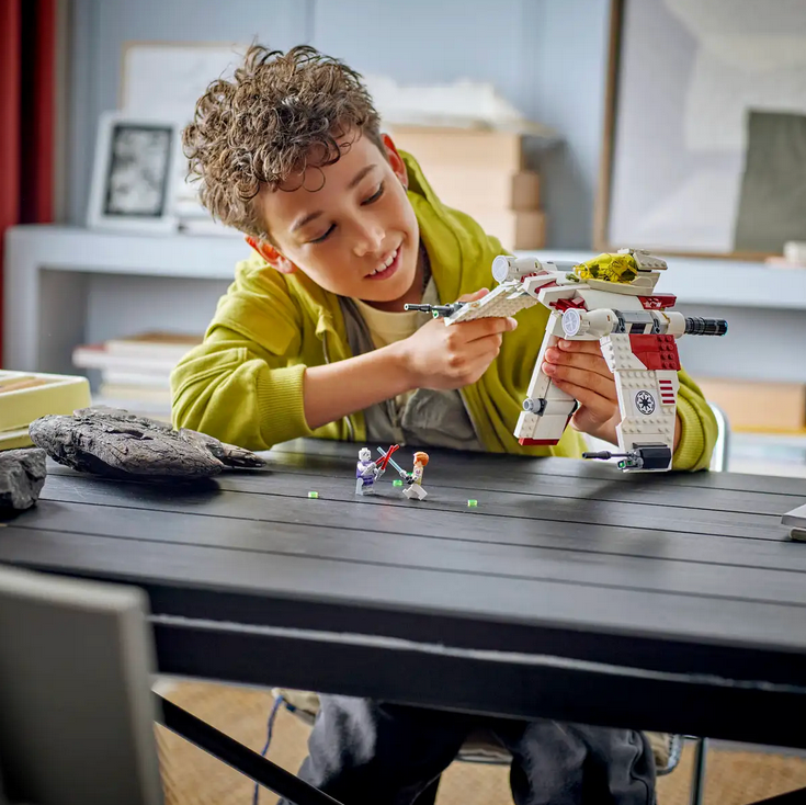 Child playing with a toy spaceship at a table in a room.
