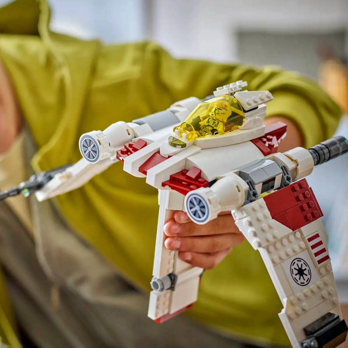 Child holding a LEGO Star Wars model in a blurred indoor setting