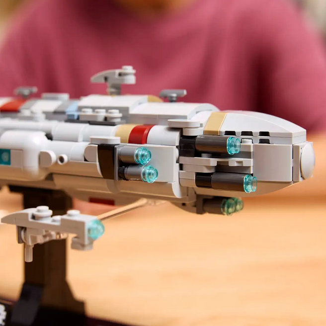 Close-up of a LEGO Star Wars spaceship model on a wooden surface with a blurred person in the background.
