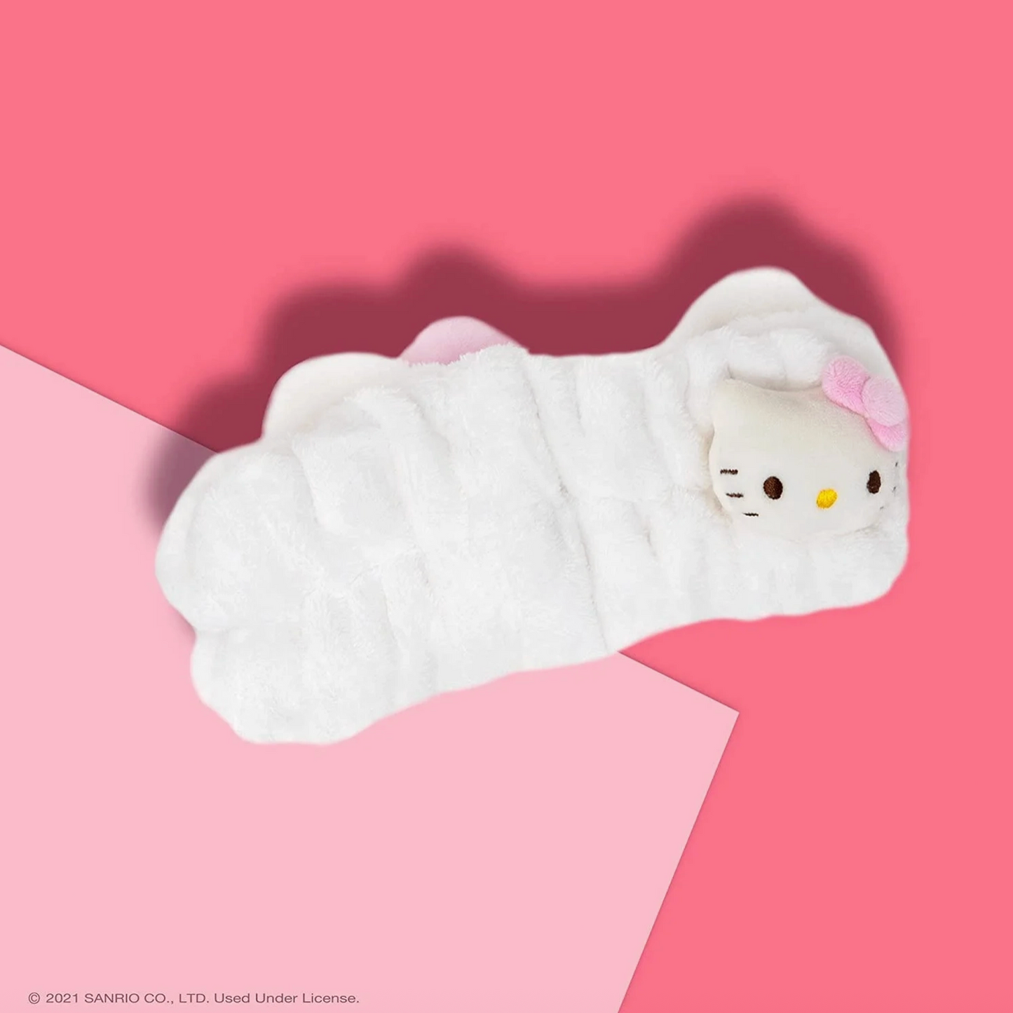 Plush toy resembling a cat character wrapped in white fabric on a pink background