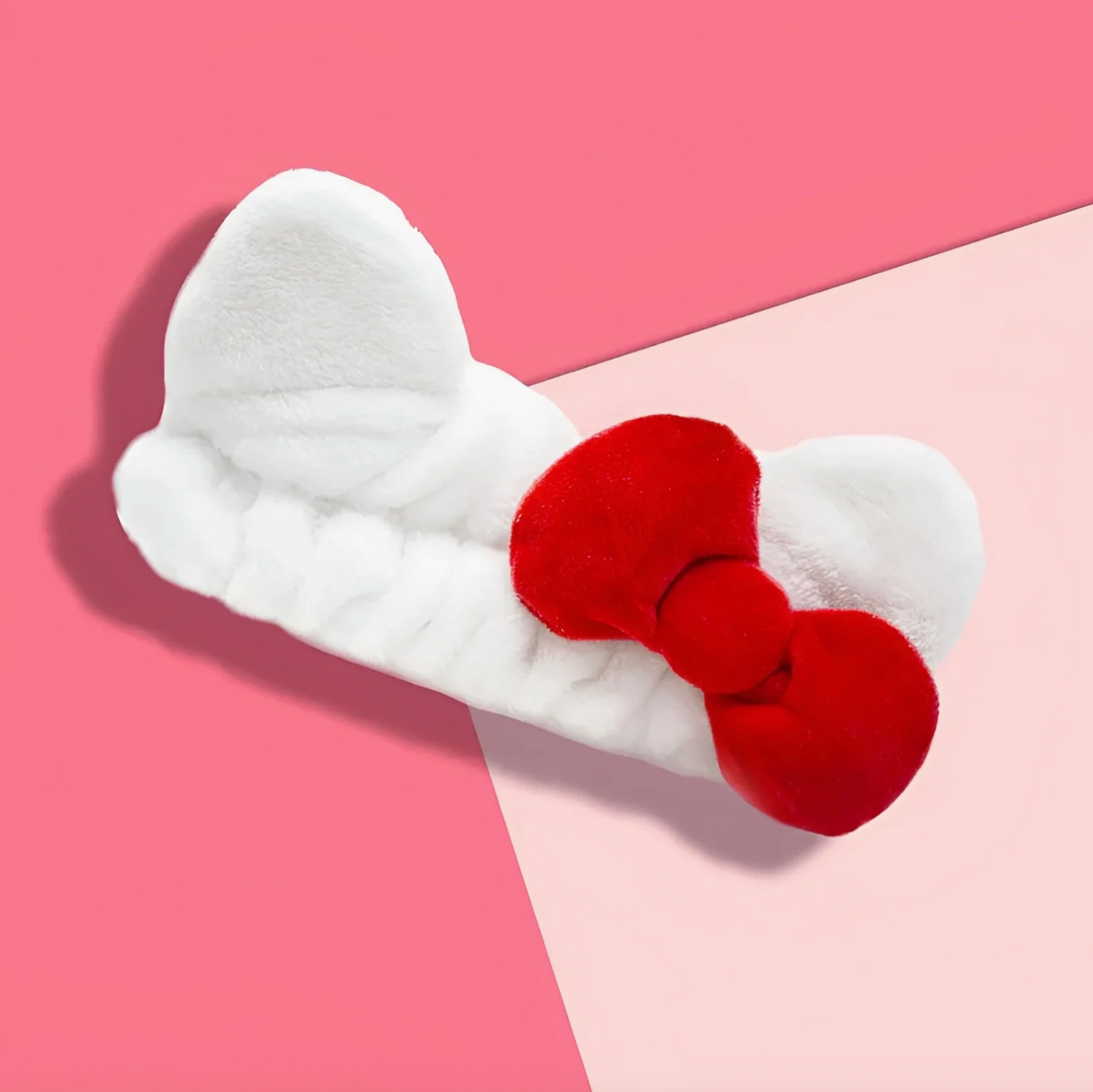 White bow-shaped hair clip with a red center on a pink background