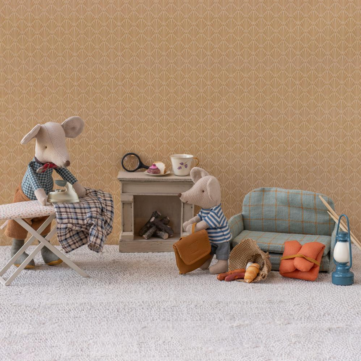 Miniature diorama with toy mice and furniture against a beige wall.