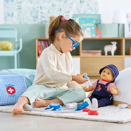 Child playing with a doll and medical kit on a rug in a room with shelves and toys.